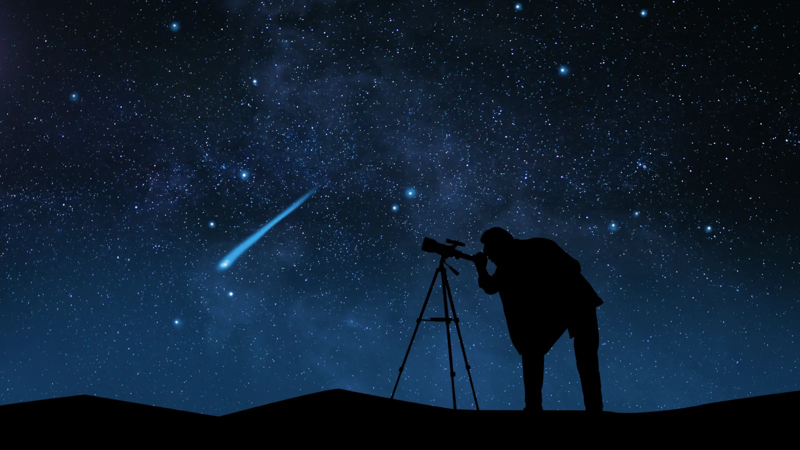 Silhouette of a photographer at a tripod as a meteor streaks across the Milky Way