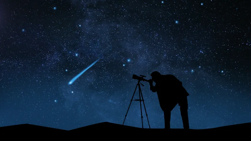 Silhouette of a photographer at a tripod as a meteor streaks across the Milky Way