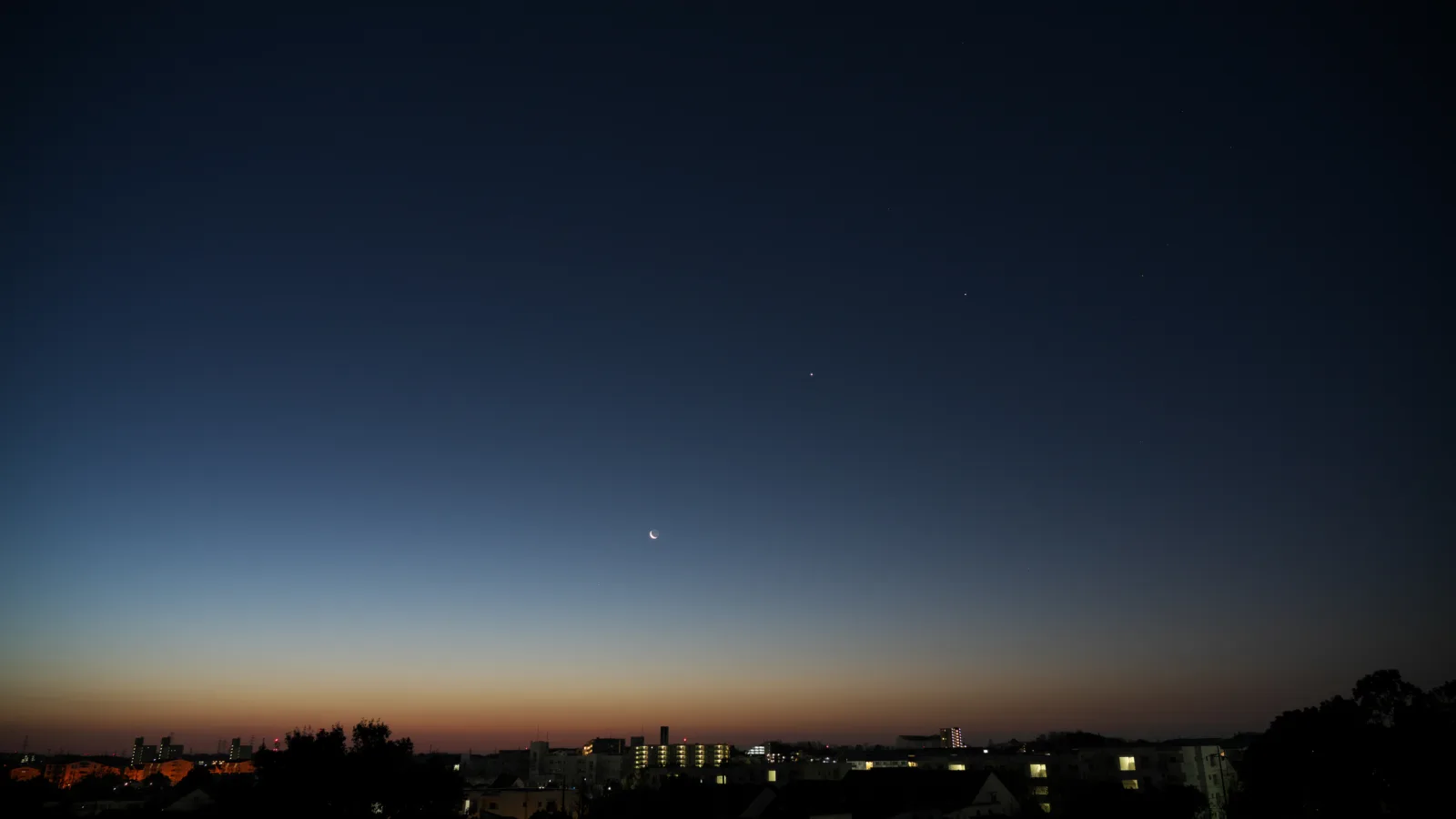 Crescent Moon and bright planets in the evening twilight over a city skyline