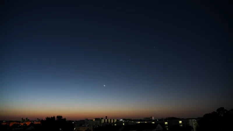 Crescent Moon and bright planets in the evening twilight over a city skyline