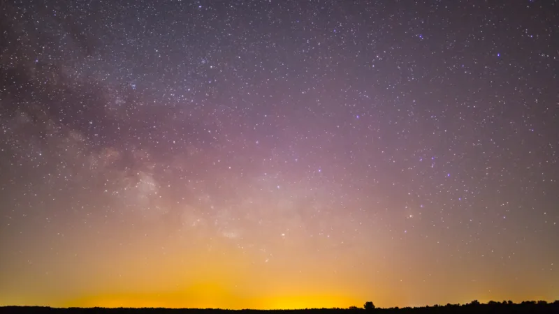 Milky Way and a faint zodiacal light glow above the horizon over dark fields